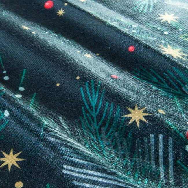 Zielono-biała ścierka kuchenna w zestawie 2 sztuki (38x60 cm) z delikatnym, świątecznym wzorem leżąca na stole. Widoczne wzory igliwia, gwiazdy i czerwone akcenty na ciemnym tle, z teksturą przypominającą tkaninę.