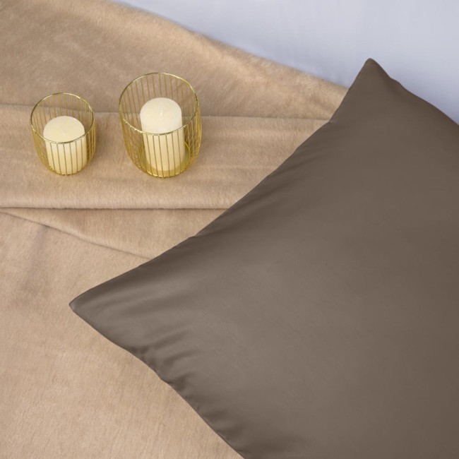 Poszewka satynowa w kolorze sepia w rozmiarze 50x80 cm, leżąca na jasnym tle. Obok znajdują się dwa małe świeczniki z metalowej siatki z białymi świecami. Kąt ujęcia z góry, podkreślający jedwabistą fakturę materiału.