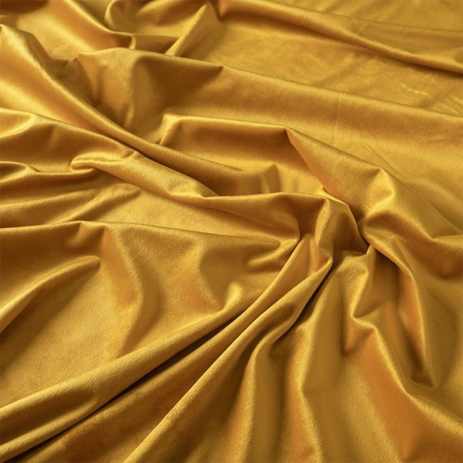 Zasłona gotowa welwetowa w kolorze szafranowym, wykonana z miękkiej tkaniny Velvi. Złożona, z widoczną fakturą i lejącym się materiałem. Ujęcie z góry, ukazujące fale tkaniny, akcentujące jej bogaty odcień i gładkość.