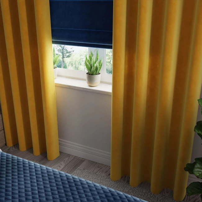Zasłona gotowa welwetowa 140x260 cm, w kolorze szafranowym, wykonana z miękkiej tkaniny Velvi, zawieszona na przelotkach. Ujęcie frontalne, z widocznym otoczeniem okna z roletą oraz doniczką z rośliną na parapecie. Tło w naturalnym świetle.