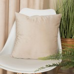 Poszewka welwetowa 40x40, jasno beżowa, leżąca na białym krześle. Produkt o gładkiej, miękkiej fakturze, bez widocznych napisów czy logo. W tle widoczna zieleń roślin, co nadaje aranżacji przytulny klimat.