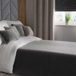 Poszewka dekoracyjna Velvi 40x40 cm w ciemnoszarym kolorze, wykonana z welwetu. Kąt ujęcia frontalny, poszewka leży na łóżku obok poduszek o różnych odcieniach szarości. W tle zasłony i okno z rośliną doniczkową. Produkt w aranżacji sypialni.