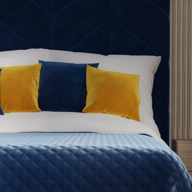 Ciemno niebieska poszewka dekoracyjna 40x40 wykonana z welwetu, leżąca na białej pościeli. W tle widnieją dwie żółte i jedna niebieska poduszka. Produkt w aranżacji sypialni, na tle strukturalnej ściany w odcieniach granatu.