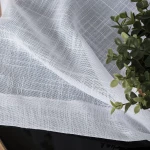 Firana na przelotkach w kolorze białym, wykonana z etaminy, o gładkiej fakturze i wymiarach 140x250 cm. Tkanina ma subtelny wzór w kratkę, leży na czarnej powierzchni obok zielonej rośliny.