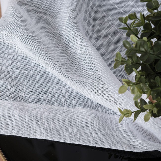 Firana na przelotkach w kolorze białym, wykonana z etaminy, o gładkiej fakturze i wymiarach 140x250 cm. Tkanina ma subtelny wzór w kratkę, leży na czarnej powierzchni obok zielonej rośliny.