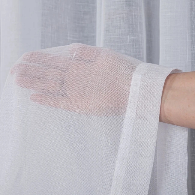 Firana gładka na przelotkach w kolorze białym, wykonana z etaminy. Widać zbliżenie na materiał, który jest lekki i półprzezroczysty, trzymany w dłoni. Długość 250 cm, szerokość 140 cm.