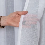 Biała firana na przelotkach z etaminy, o wymiarach 140x250 cm, z widoczną ręką trzymającą materiał. Tkanina jest lekka i półprzezroczysta, z gładką fakturą oraz białą lamówką po brzegach, co podkreśla jej elegancki wygląd.