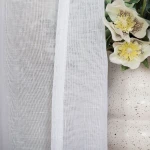 Firana na przelotkach w kolorze białym, wykonana z etaminy, o wymiarach 140x250 cm. Tkanina gładka, lekka i transparentna, zwisająca obok doniczki z kwiatami. Ujęcie z boku, ukazujące detale materiału oraz krawędź firany.