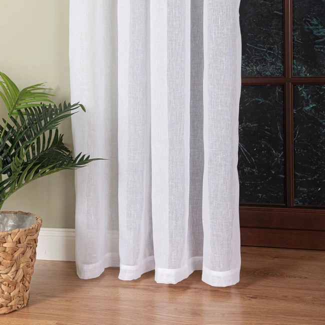 Firana na przelotkach, gładka, w kolorze białym, wykonana z etaminy, o wymiarach 140x250 cm. Ułożona wzdłuż okna, z widocznymi detalami wykończenia na dole, obok doniczki z zieloną rośliną i drewnianym tłem.