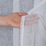 Firana na przelotkach w kolorze białym z etaminy, o wymiarach 140x250 cm. Widać delikatną strukturę materiału oraz rękę trzymającą brzeg firany. Tło jest jednolite, co podkreśla lekkość i przejrzystość tkaniny.