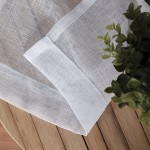 Biała firana na przelotkach z etaminy, gładka, o wymiarach 140x250 cm. Ujęcie z bliska, pokazujące teksturę materiału oraz wykończenie brzegów. W tle widoczna roślina doniczkowa, na jasnej drewnianej powierzchni.
