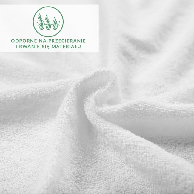 Prześcieradło frotte 160x200 w kolorze białym leży na stole. Zbliżenie ukazuje teksturę materiału, który jest miękki i gładki. Na zdjęciu znajduje się zielony napis informujący o odporności na przecieranie. Tło jest jasne i neutralne.