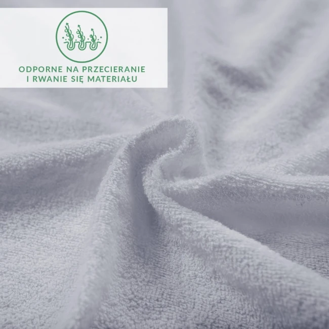 Frotte prześcieradło w kolorze popielatym o wymiarach 200x220 cm, ukazane z bliska w lekkim skręcie. Widać teksturę materiału, który jest miękki i gładki. Widoczne logo oraz informacje o odporności na przecieranie i rwanie materiału.