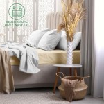 Prześcieradło frotte z gumką 180x200 w jasnym beżu, rozłożone na łóżku. Widoczne poduszki w kolorze szaro-białym. Obok stoliczek z wazonem i roślinnością, leżący pled w jasnym odcieniu. Tło neutralne, stonowane, w aranżacji sypialnianej.