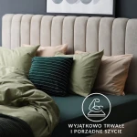 Prześcieradło jersey z gumką 120x200 w kolorze białym leży na łóżku, w otoczeniu kolorowych poduszek w odcieniach zieleni i beżu. Widoczne detale to gładka faktura materiału oraz gumka zabezpieczająca. Na tle beżowego zagłówka.