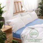 Prześcieradło jersey z gumką w kolorze niebieskim, rozmiar 160x200, leży na łóżku. Produkt z gładkiej, elastycznej tkaniny, idealnie przylega do materaca.