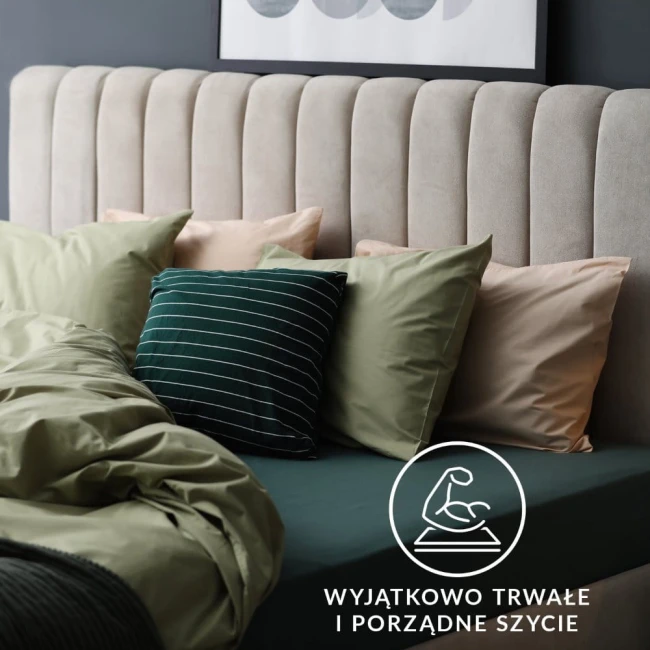 Prześcieradło jersey z gumką w kolorze popielatym, rozmiar 200x220 cm, leży na łóżku z miękkimi poduszkami w odcieniach zieleni i beżu. W tle widoczna jest tapicerowana głowa łóżka, a na zdjęciu umieszczono logo z informacją o trwałym szyciu.