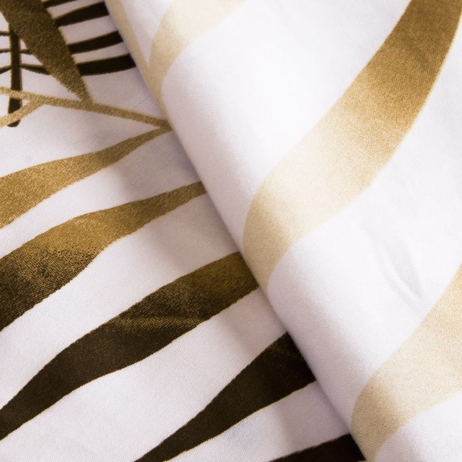 Pościel satyna bawełniana 220x200 w białym kolorze z beżowym wzorem liści. Materiał o gładkiej fakturze, leżąca, złożona w połowie, na jasnym tle. Widać duże, stylizowane liście oraz miękkie krawędzie poszwy.