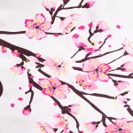Pościel satyna bawełniana 180x200 z białym tłem, zdobiona różowymi kwiatami wiśni. Wzór pokazuje gałęzie z kwiatami i pąkami. Materiał jest gładki i lśniący. Produkt leży na płaskiej powierzchni, ukazując detale wzornictwa.