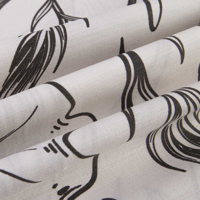 Pościel satyna bawełniana 160x200 w białym kolorze z czarnymi konturowymi kwiatami i liśćmi, złożona w sposób ukazujący detale wzoru i tekstury materiału. Ujęcie w zbliżeniu, ukazujące delikatność wykończenia i fakturę tkaniny.