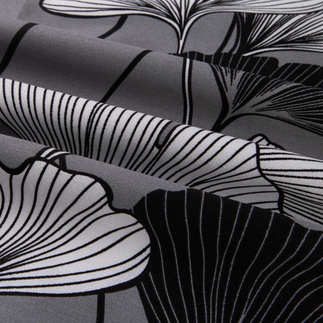 Pościel satynowa bawełniana 200x220 cm w kolorze białym z czarno-białym wzorem liści miłorzębu. Materiał gładki, z wyraźnym nadrukiem, ułożona w delikatne fałdy, ukazując detale wzoru i teksturę tkaniny.