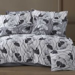 Pościel satyna bawełniana 200x220 cm w kolorze białym z motywem czarno-białych liści miłorzębu. Zestaw zawiera poszewki na poduszki oraz narzutę. Materiał gładki, z delikatnym wzorem, ułożony na łóżku z ciemnym tłem.
