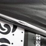 Pościel satyna bawełniana 140x200 z szaro-białymi pasami w ornamenty, z widocznym zamkiem błyskawicznym. Produkt leży na jaśniejszym tle, ukazując szczegóły wzoru oraz fakturę materiału. Widać również jasne wykończenie zamka.
