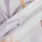 Zbliżenie na pościel satynową w kolorze białym z szaro-beżowymi liśćmi, ukazujące zamek błyskawiczny. Wzór liści jest delikatny i subtelny, a tkanina ma gładką, matową fakturę. Widoczne w kolorze białym detale zamka.