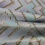 Pościel satynowa w rozmiarze 200x220 cm w błękitnym kolorze z szarym geometrycznym wzorem. Materiał z delikatnym połyskiem, złożony w falach, eksponujący wzory w kształcie zygzaków i linii.