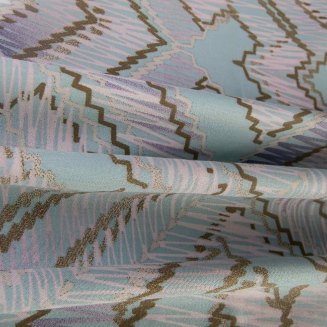 Pościel satynowa w rozmiarze 200x220 cm w błękitnym kolorze z szarym geometrycznym wzorem. Materiał z delikatnym połyskiem, złożony w falach, eksponujący wzory w kształcie zygzaków i linii.