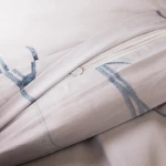 Pościel satyna bawełniana 220x200 cm w jasnym odcieniu z pastelowymi błękitnymi kwiatkami. Zamek błyskawiczny w poszewce. Materiał gładki, z delikatnym nadrukiem. Produkt leżący, ukazujący detal zamka i wzór.