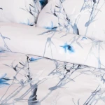 Pościel satyna bawełniana 160x200 w jasnym tle z pastelowymi błękitnymi kwiatkami. Wzór floralny z delikatnymi gałązkami, materiał gładki, złożona pościel z poduszkami tworzy harmonijną kompozycję.