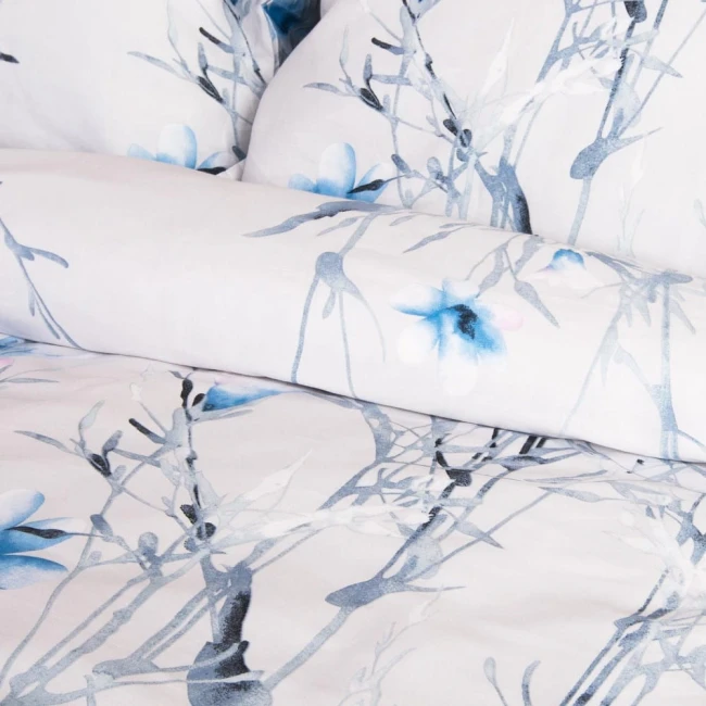 Pościel satyna bawełniana 160x200 w jasnym tle z pastelowymi błękitnymi kwiatkami. Wzór floralny z delikatnymi gałązkami, materiał gładki, złożona pościel z poduszkami tworzy harmonijną kompozycję.