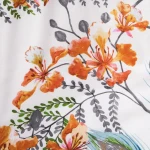 Pościel bawełniana 140x200 Cottonlove w białym kolorze z tropikalnym wzorem w pomarańczowe kwiaty i zielone liście. Materiał gładki, z wyraźnym nadrukiem. Ujęcie z bliska, ukazujące detale wzoru.