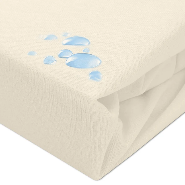 Ochronne prześcieradło z gumką w kolorze kremowym, z widocznymi kroplami wody na powierzchni materiału. Produkt leży na płaskiej powierzchni, z wyraźną teksturą tkaniny. Idealne do ochrony materaca w rozmiarze 140x200 cm.