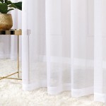 Firana gotowa na srebrnych przelotkach, biała, wykonana z lekkiego materiału. Zawieszona w pionie, z widocznym detalem przelotek. Tło w jasnych odcieniach, z rośliną w złotej doniczce na metalowym stoliku oraz dywanem, co tworzy przytulny klimat.