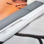 Zbliżenie na poszewkę pościeli satynowej w kolorze szaro-pomarańczowym z wzorem kwiatowym. Widoczny suwak w jasnym kolorze, materiał o gładkiej fakturze. Część poszewki z motywem kwiatowym oraz stonowana dolna część.