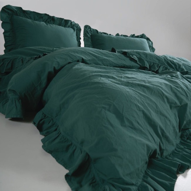 Pościel bawełniana w kolorze zieleni butelkowej z falbanką, rozłożona na łóżku. Zestaw zawiera dwa poduszki z falbankami. Materiał jest gładki, a całość ma rozmiar 220x200 cm. Tło jest jasne, co podkreśla kolor pościeli.