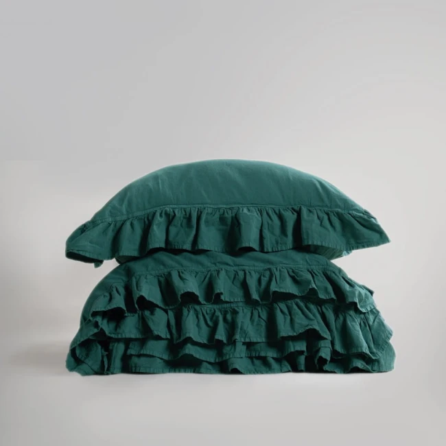 Pościel bawełniana z falbanką w kolorze ciemnozielonym, 220x200 cm, leżąca na sobie poduszka z falbanką. Tło proste, szare. Widoczne detale falbany oraz tekstura materiału, który jest gładki.