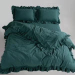 Pościel bawełniana z falbanką 220x200 w kolorze zieleni butelkowej, składająca się z narzuty i dwóch poduszek. Ułożona na łóżku, z widoczną falbana na brzegach. Tło jasne, co podkreśla głęboki odcień. Zestaw zawiera komplet pościeli dla dwóch osób.