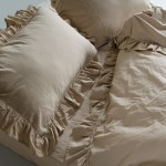 Pościel bawełniana z falbanką w kolorze beżowym, rozmiar 220x200 cm, składająca się z poszewek na poduszki z dekoracyjnym obszyciem oraz kołdry. Ułożona na łóżku, w zbliżeniu ukazuje teksturę materiału oraz falbanki przy brzegach.