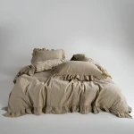 Pościel bawełniana z falbanką 220x200 Stonewashed Exclusive, Oxfordtan, beżowa, rozłożona na łóżku. Widoczne poduszki z falbanką, w jednolitym, matowym kolorze. Tło jasne, minimalistyczne, podkreślające teksturę materiału.