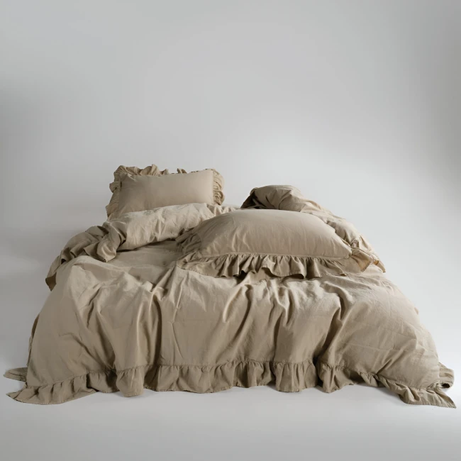 Pościel bawełniana z falbanką 220x200 Stonewashed Exclusive, Oxfordtan, beżowa, rozłożona na łóżku. Widoczne poduszki z falbanką, w jednolitym, matowym kolorze. Tło jasne, minimalistyczne, podkreślające teksturę materiału.