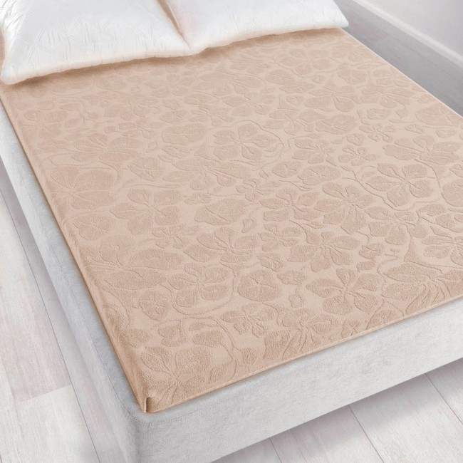 Prześcieradło żakardowe bez gumki o wymiarach 150x205 cm w jasnym beżowym kolorze, leżące na łóżku. Materiał ma delikatny, teksturowany wzór roślinny. Tło neutralne, podkreślające kolor i fakturę produktu. Widoczne poduszki w białych poszewkach.