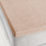 Prześcieradło żakardowe w kolorze jasny beż, o wymiarach 175x220 cm, wykonane z miękkiego materiału z subtelnym wzorem roślinnym. Produkt leży na materacu, co ukazuje jego fakturę i detale. Ujęcie z boku, na jasnym tle.