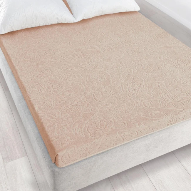 Prześcieradło żakardowe bez gumki w kolorze jasnego beżu, o wymiarach 175x220 cm, ułożone na łóżku. Wzór z wysublimowanymi detalami roślinnymi, lekko teksturowana powierzchnia. W tle widoczne jasne poduszki oraz łóżko o szarym kolorze.