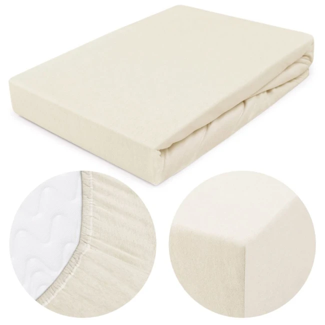 Prześcieradło jersey z gumką o wymiarach 180x200 cm w kolorze ecru, leżące na płaskiej powierzchni. Zbliżenie na fakturę materiału i detale gumki, zapewniające mocne trzymanie. Prosty, neutralny design, idealne do sypialni.