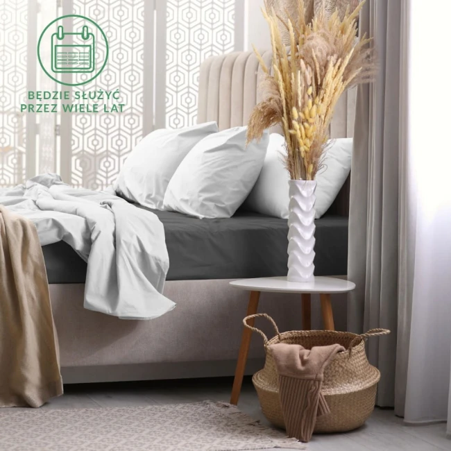 Prześcieradło frotte z gumką 180x200 w kolorze ciemnym szarym, umieszczone na łóżku z białymi poduszkami. Ułożone leżąco z widoczną teksturą materiału.