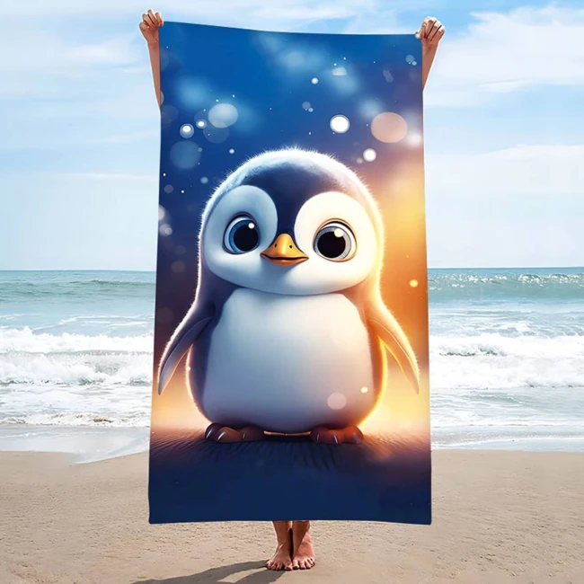 Ręcznik plażowy 100x180 cm z mikrofibry przedstawiający pingwinka, trzymany przez osobę stojącą na plaży. Tło to morze i niebo, a materiał w kolorze niebieskim z dużym, kolorowym wzorem pingwinka. Szybkoschnący, biznesowy o dużych wymiarach.