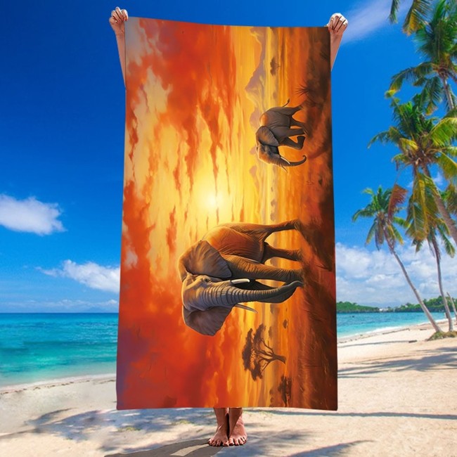 Ręcznik plażowy 100x180 cm z mikrofibry, przedstawiający słonie na tle zachodzącego słońca. Produkt jest trzymany w pionie, na plaży, z turkusowym morzem w tle. Wzór jest pełen kolorów, od pomarańczowego do żółtego. Idealny na plażę.